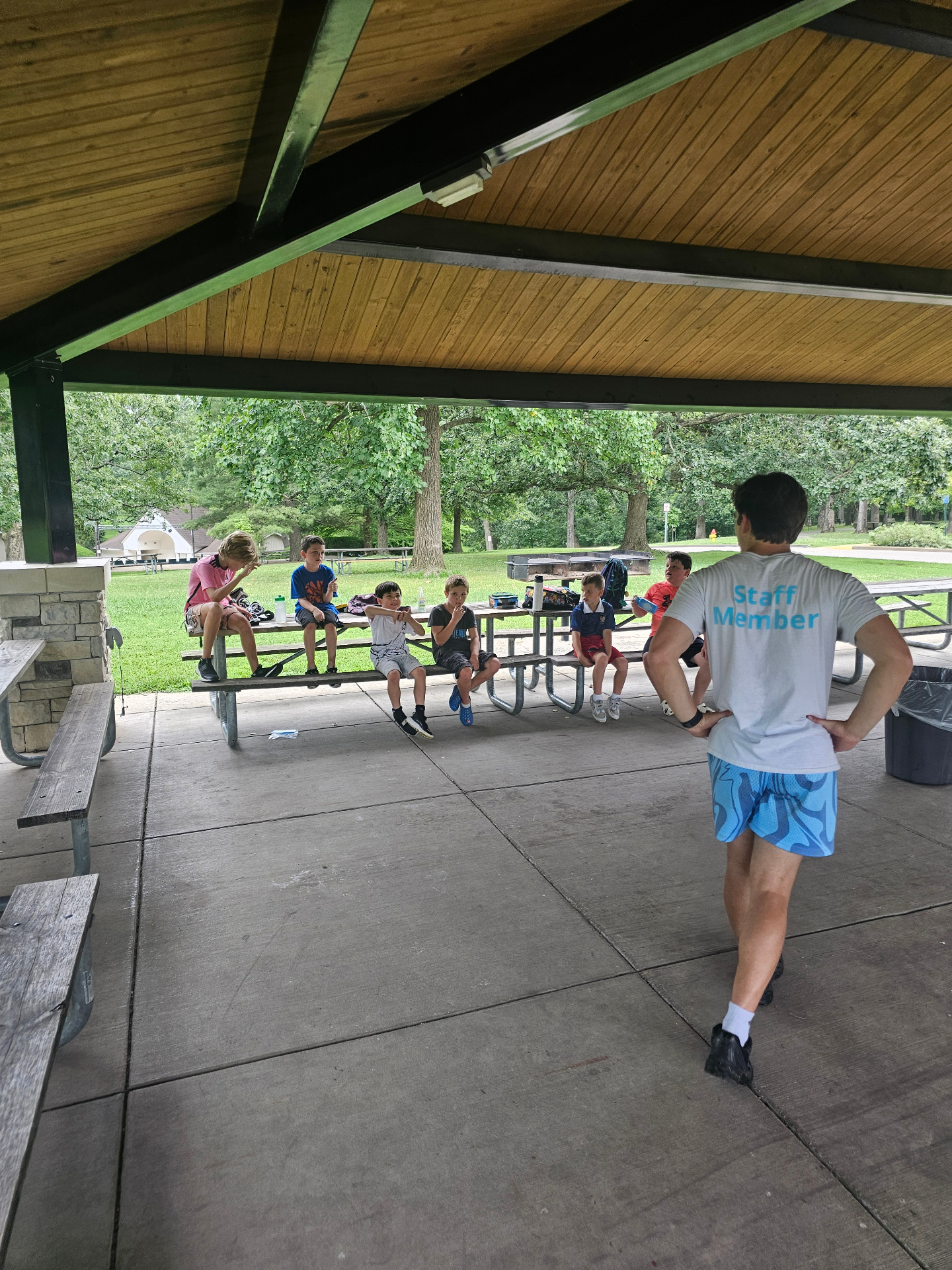 A staff member leading a group of campers at a park pavilion
